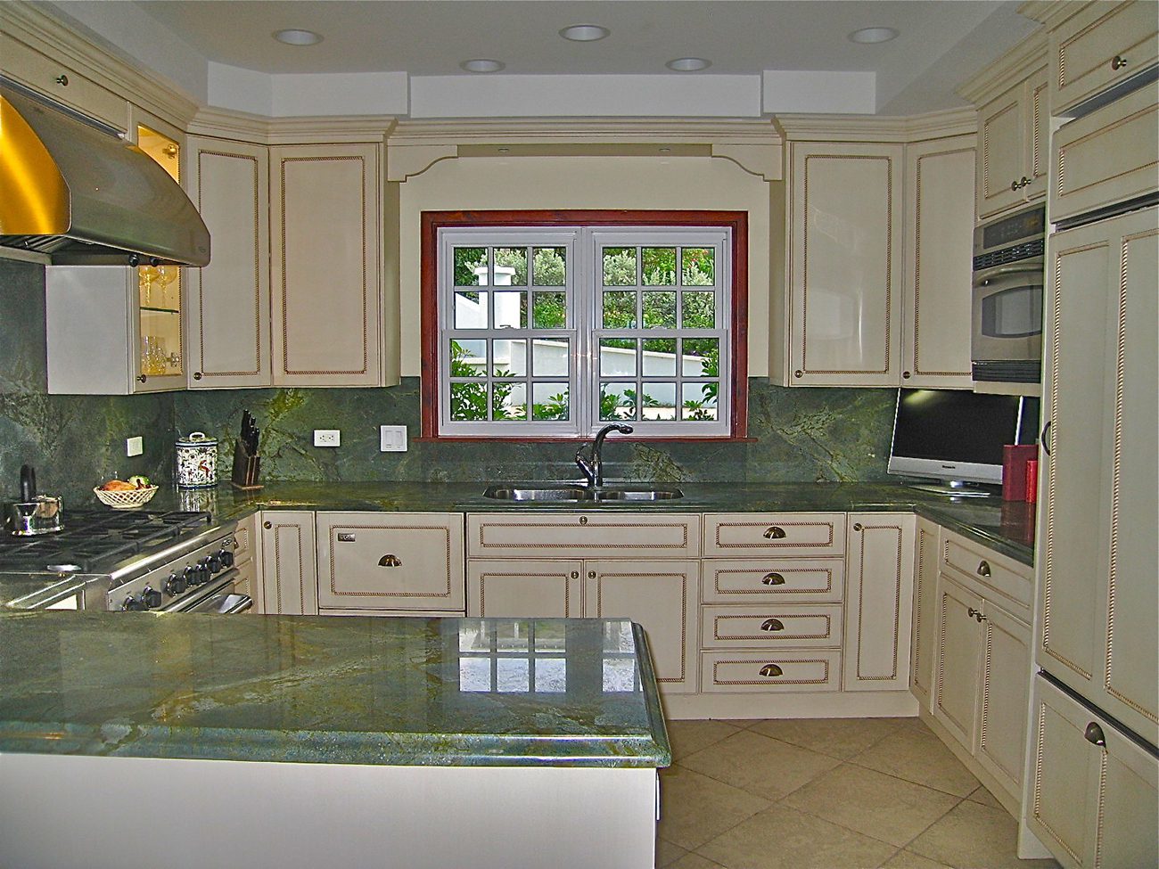 A kitchen with green marble counter tops and white cabinets.