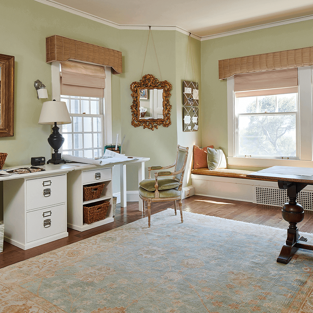 A living room with a desk and chair, a window seat, and a large mirror.